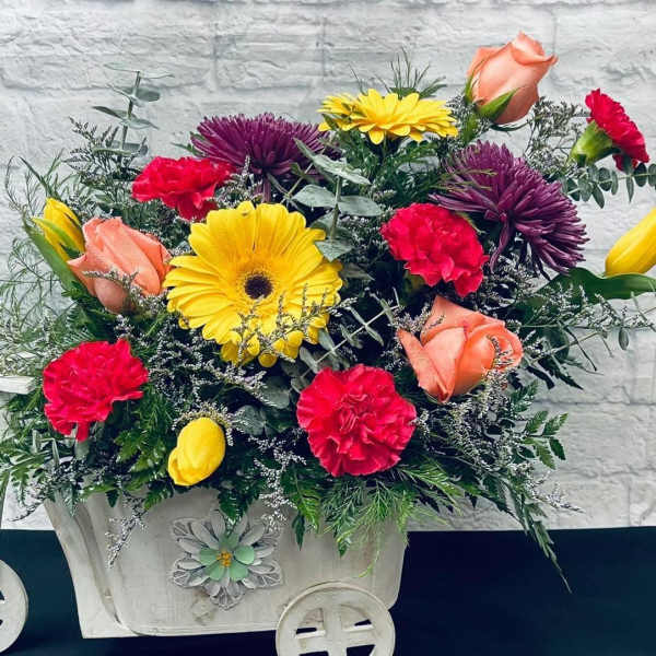 Mixed bouquet in a white decorative cart with yellow, pink, and peach blooms