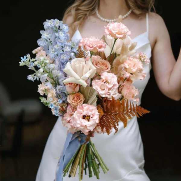 Bride holding a pastel bouquet with roses, carnations, and blue flowers