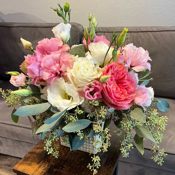 Pink and white bouquet in a square vase with trailing greenery