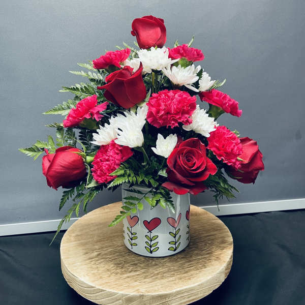 Red roses and pink carnations with white daisies in a heart-patterned vase