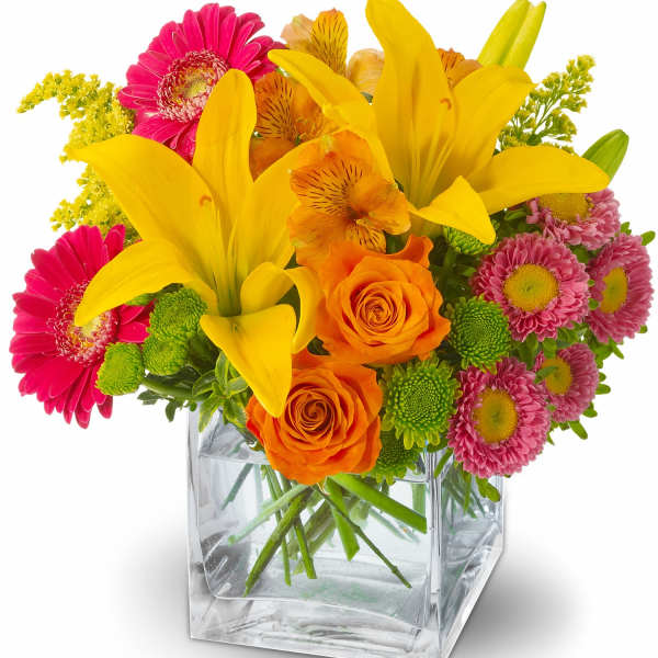 Bright mixed bouquet in a clear square glass vase with yellow lilies and pink daisies