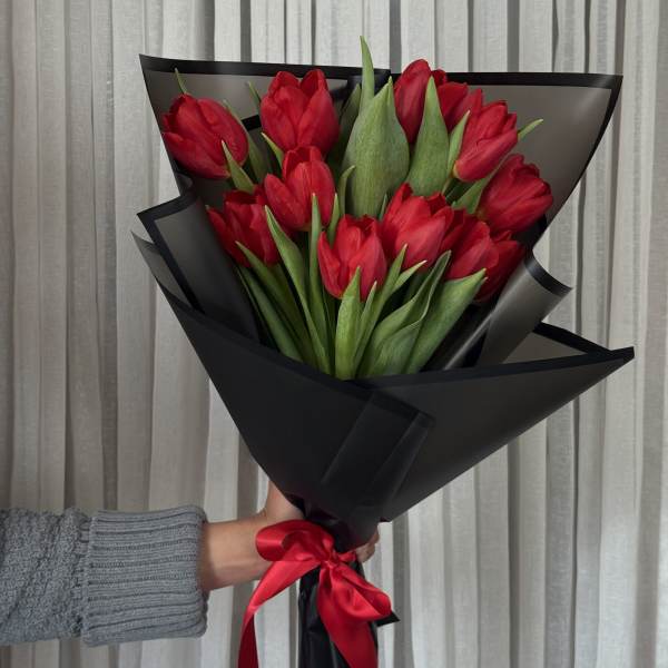 Bouquet of red tulips wrapped in black paper with a red ribbon
