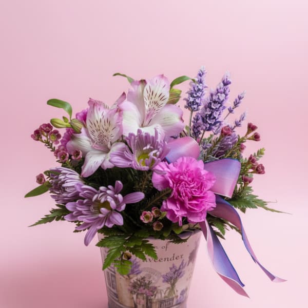 Lavender and pink flower arrangement in a decorative tin container with ribbon