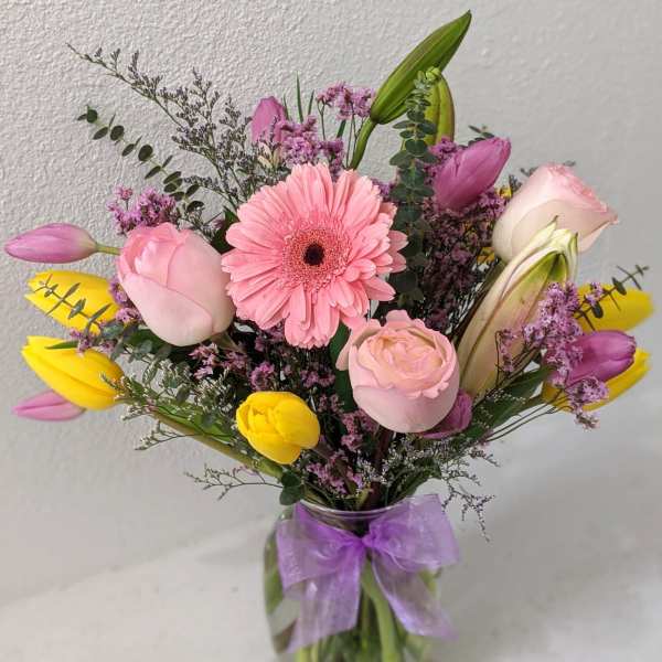 Pink and yellow mixed bouquet in a glass vase with a purple ribbon