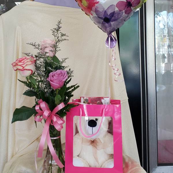 Roses in a glass vase with a Mother's Day balloon and teddy bear gift bag