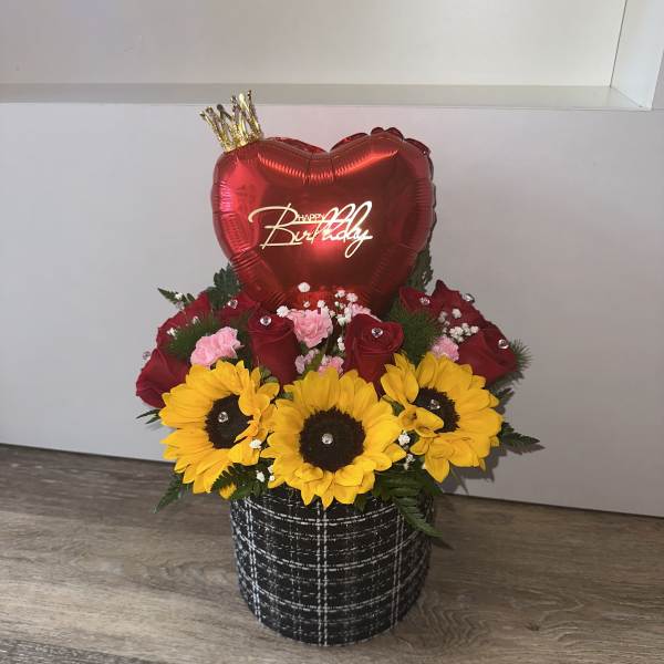 Birthday flower arrangement with sunflowers, red roses, and a heart balloon in a black container