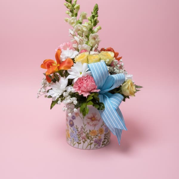 Mixed flower arrangement in a floral tin with a blue ribbon