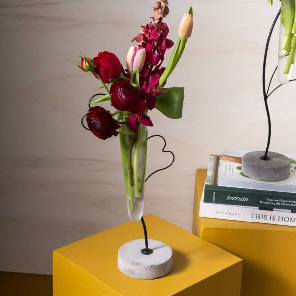 Tall modern bud vase on stand with red and pink blooms and tulips on a yellow pedestal