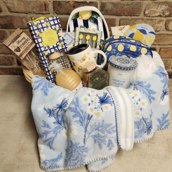 Gift basket with lemon-themed items, a mug, candle, honey, and a blanket