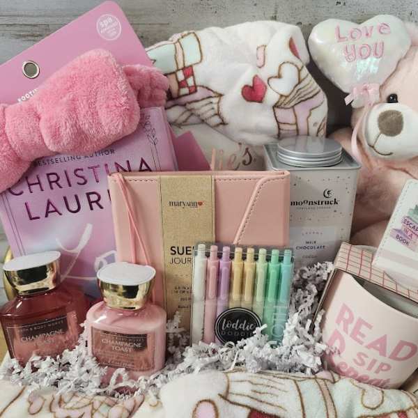 Pink gift basket with a teddy bear, candles, book, and stationery items