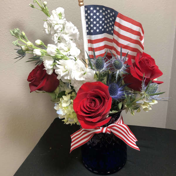 Red roses and white flowers arranged in a vase with an American flag