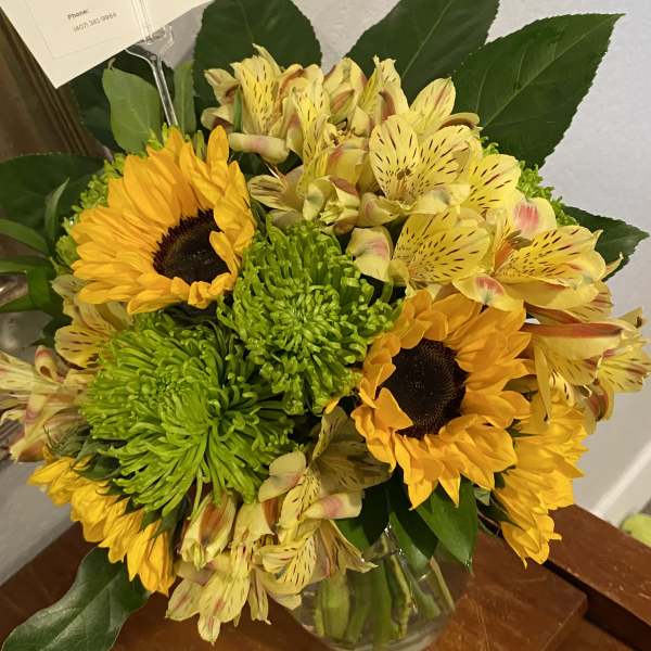 Bouquet of sunflowers, green chrysanthemums, and yellow alstroemeria in a glass vase
