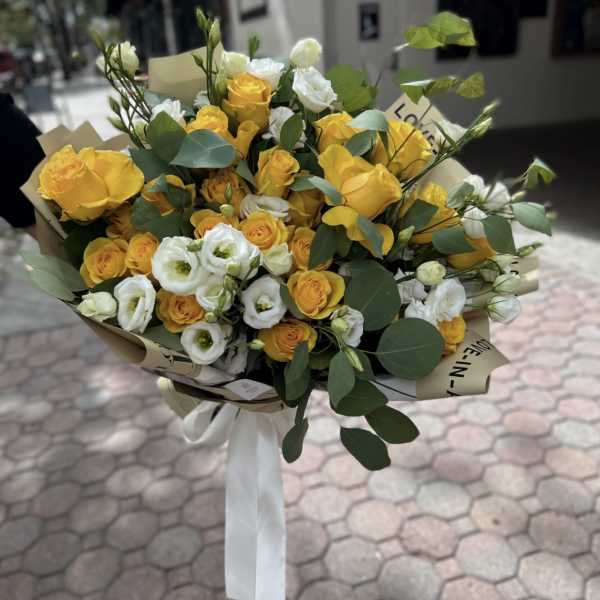 Bouquet of yellow and white roses with greenery wrapped in paper