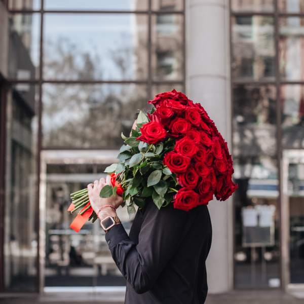 Person holding a large bouquet of red roses with orange ribbon