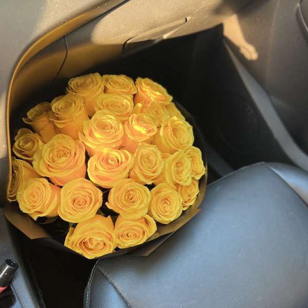 Bouquet of yellow roses wrapped in dark paper on a car seat