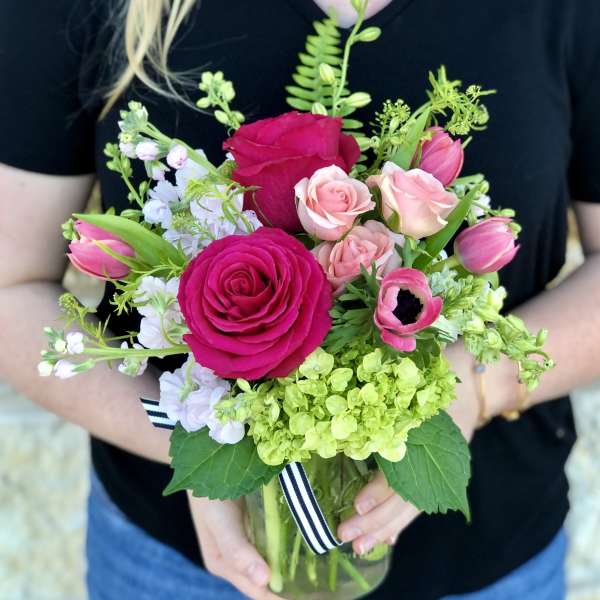 Handheld bouquet of pink roses, tulips, and white blooms in a glass vase