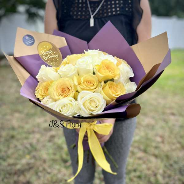 Bouquet of yellow and white roses wrapped in purple and tan paper