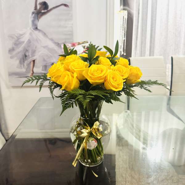 Yellow roses in a glass vase with a gold ribbon