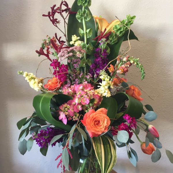Tall mixed flower arrangement in a glass vase with orange and pink blooms