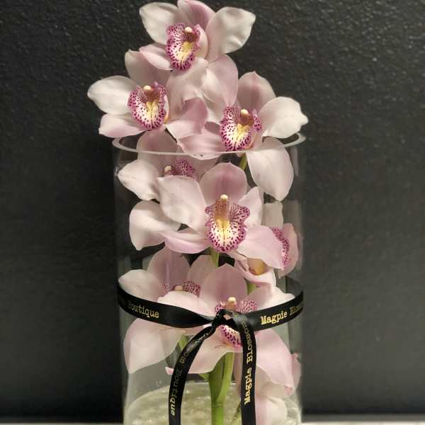 Pink orchids arranged in a clear cylinder vase with pearl beads