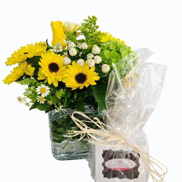Yellow flower arrangement in a glass cube vase with a wrapped gift box beside it