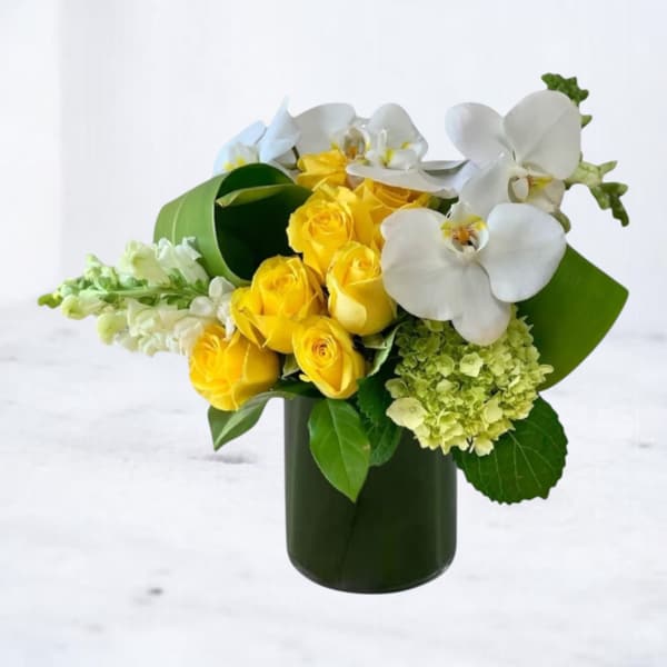 Yellow roses and white orchids arranged in a dark green vase
