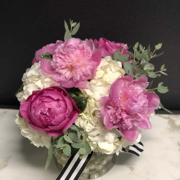 Pink peonies and white hydrangeas in a glass vase with a striped ribbon