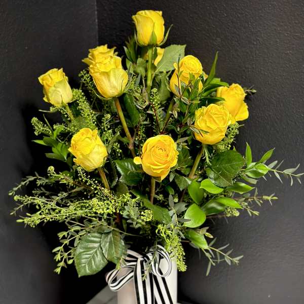 Yellow roses arranged in a white vase with a black-and-white ribbon