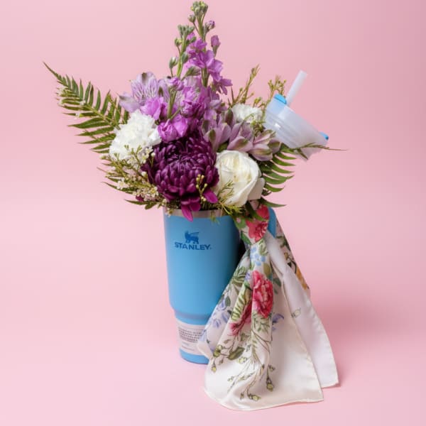 Purple and white flowers arranged in a blue tumbler with a floral scarf