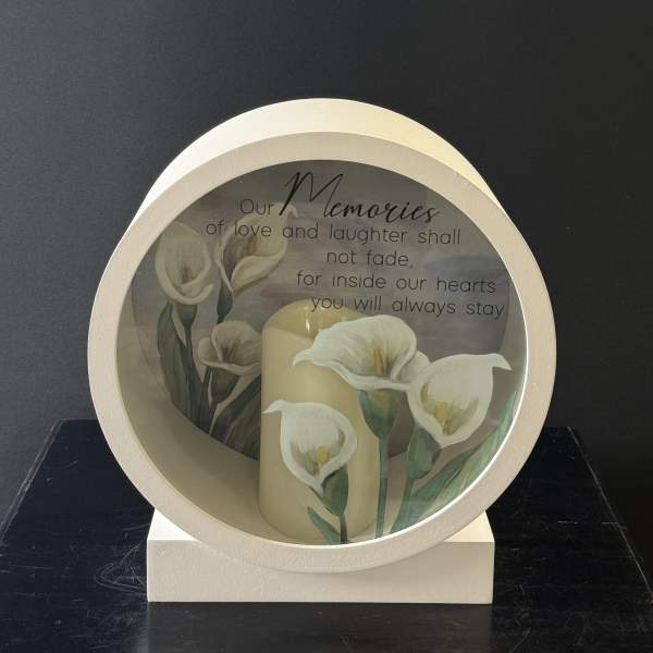 Memorial candle display with white calla lilies and a remembrance message
