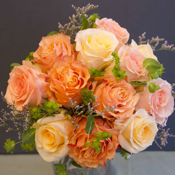 Bouquet of peach, pink, and cream roses with small purple filler flowers