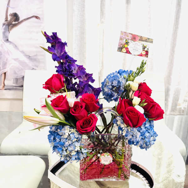 Mixed bouquet of red roses, blue hydrangeas, and purple flowers in a glass vase