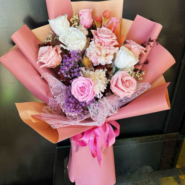 Pink and white rose bouquet wrapped in pink paper with a ribbon