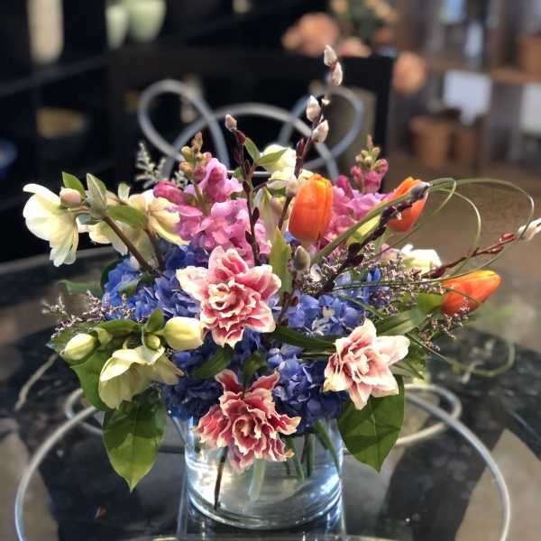 Mixed bouquet in a clear glass vase with blue, pink, orange, and white flowers
