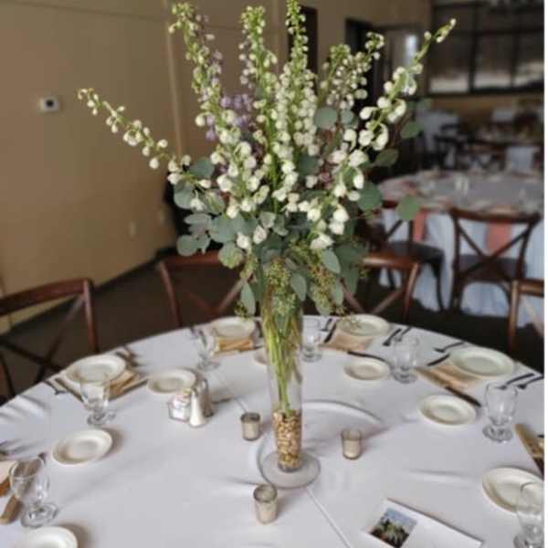 Tall white floral centerpiece in a clear glass vase on a round table