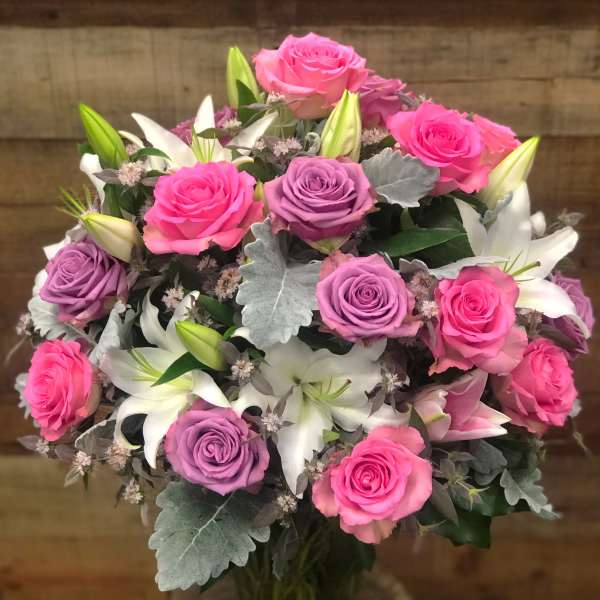 Bouquet of pink and lavender roses with white lilies in a glass vase