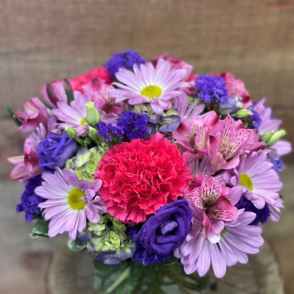 Mixed bouquet of pink, purple, and lavender flowers in a glass vase