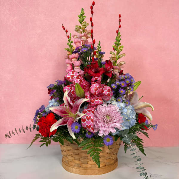Basket arrangement with pink, red, and purple flowers and heart ribbon