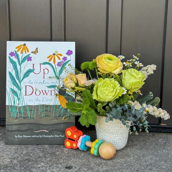 Children's book with yellow and green flower arrangement in a white pot and colorful wooden rattle.