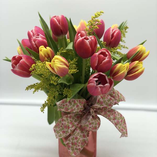 Pink and yellow tulips in a pink vase with a floral ribbon