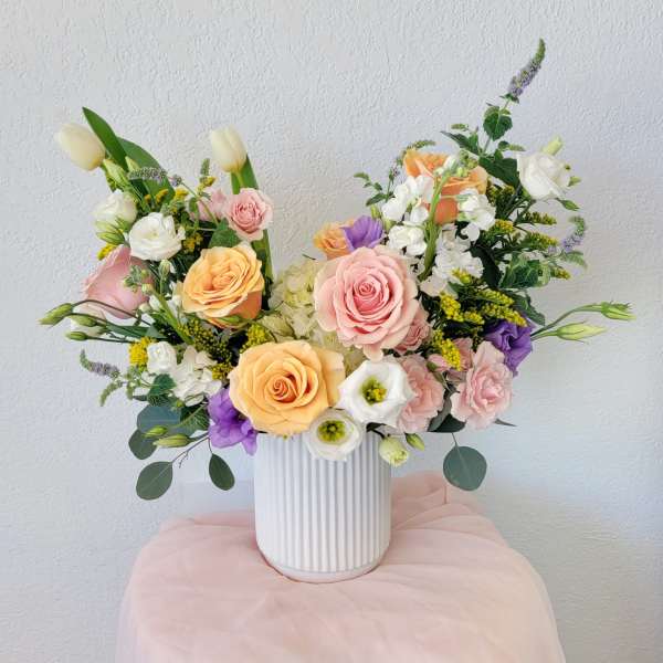 Mixed bouquet of pastel roses, tulips, and white blooms in a white vase