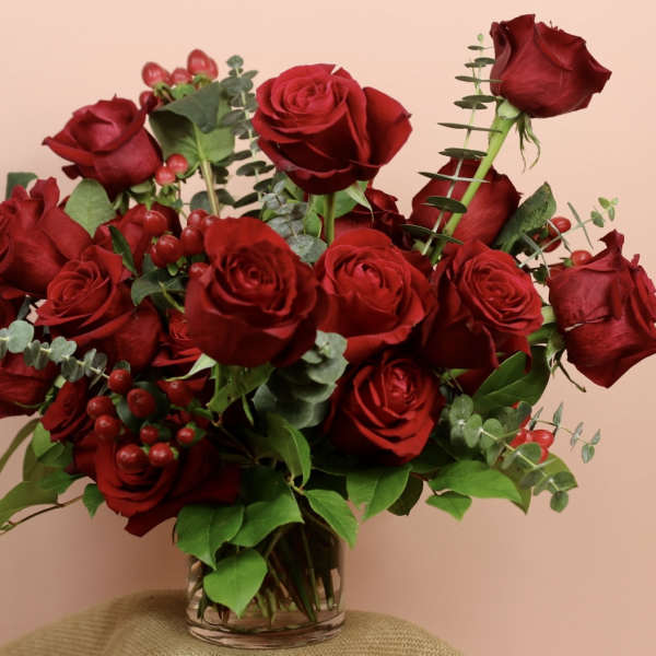 Red roses arranged in a clear glass vase with eucalyptus and berries