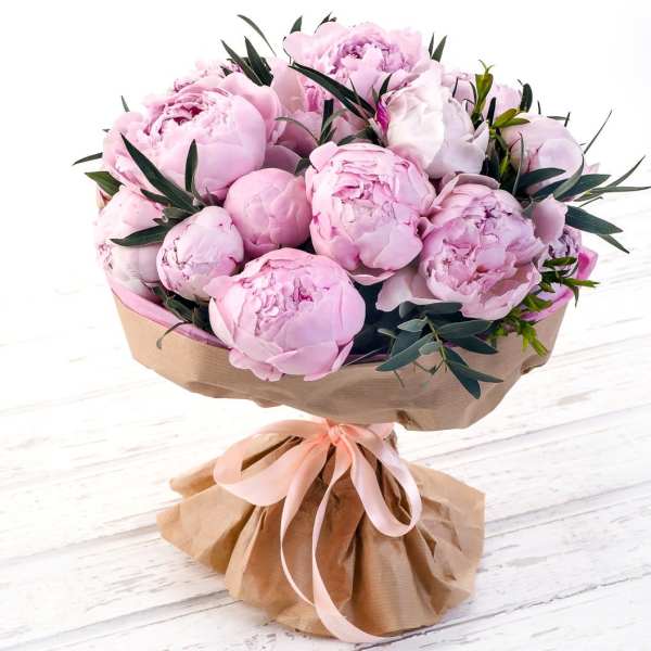 Bouquet of pale pink peonies wrapped in brown paper with a pink ribbon