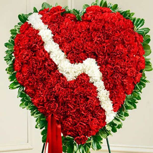 Standing red carnation heart wreath with white zigzag stripe and greenery border on an easel
