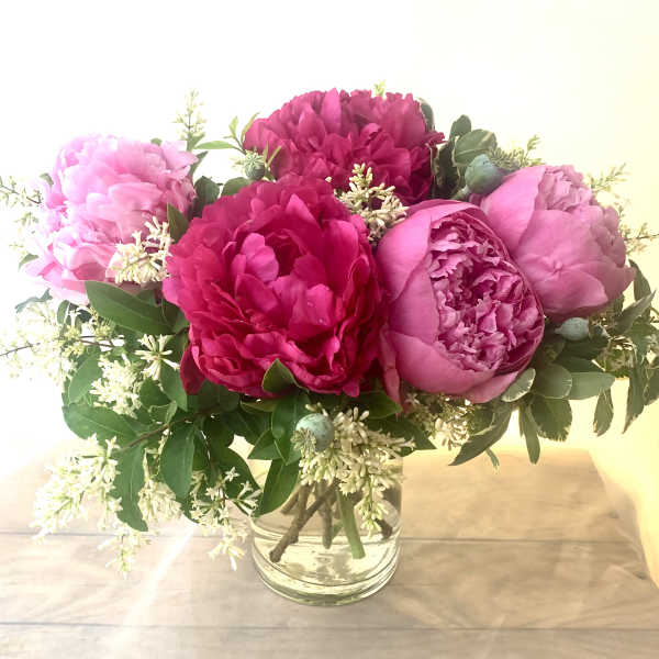 Pink peonies arranged in a clear glass vase with white filler flowers