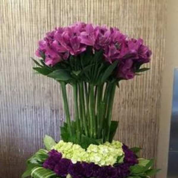 Tall purple and green floral arrangement in a silver vase