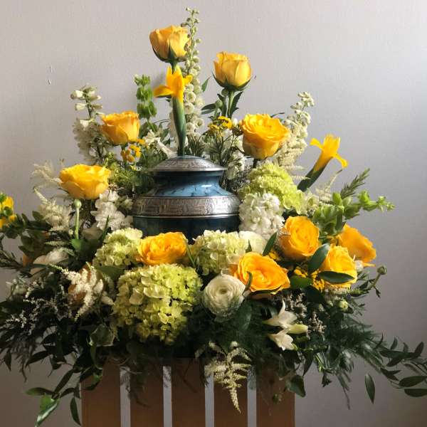 Yellow roses and white flowers arranged around a blue urn