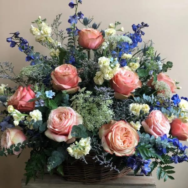 Basket arrangement of peach roses with blue and white flowers