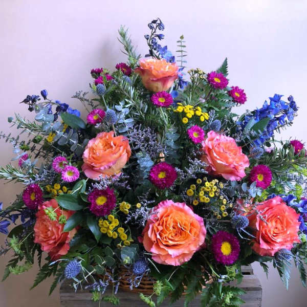Large mixed bouquet with orange roses and blue flowers in a basket