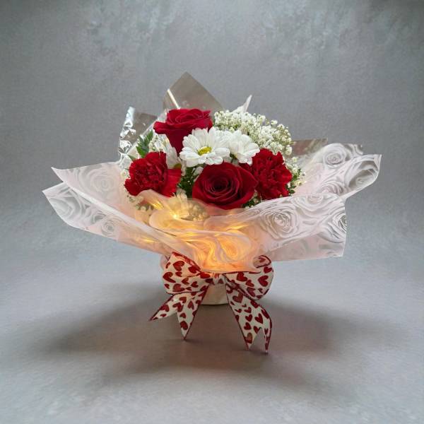 Red roses and white daisies in a wrapped bouquet with a heart-patterned bow